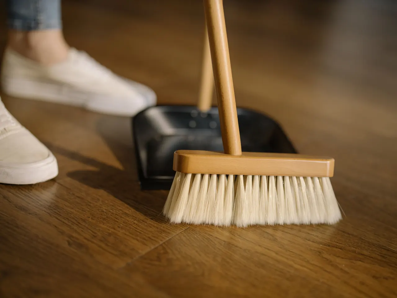 A broom and dustpan used to clean a wood floor